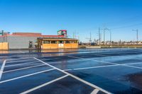 a parking lot with a pizza store near an intersection on a rainy day under a blue sky