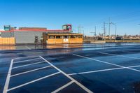 a parking lot with a pizza store near an intersection on a rainy day under a blue sky