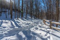 snow covered path with wooden fence on the side of a hill at winter time, with sun streaming through