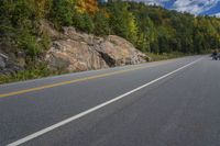 a black motorcycle is going down a highway in the woods of a mountain pass with the mountains beyond