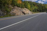 a black motorcycle is going down a highway in the woods of a mountain pass with the mountains beyond