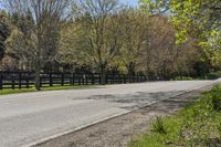 a car driving down a rural road past a fence and trees at the end of a road