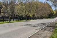 a car driving down a rural road past a fence and trees at the end of a road