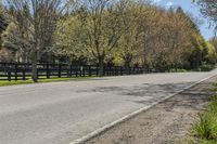 a car driving down a rural road past a fence and trees at the end of a road