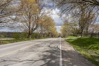 a road with some grass and trees next to the road with blue sky and clouds behind it