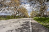 a road with some grass and trees next to the road with blue sky and clouds behind it