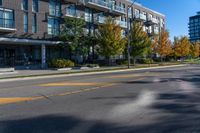 a empty city street next to an apartment building in fall season, with yellow painted markings