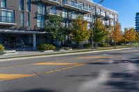 a empty city street next to an apartment building in fall season, with yellow painted markings