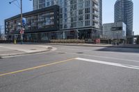 there is a bike going down the street in front of a large building, while an empty parking lot stands at the curb