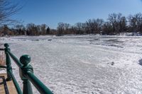 a lake filled with lots of ice near a fence with a bench sitting next to it