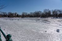 a lake filled with lots of ice near a fence with a bench sitting next to it