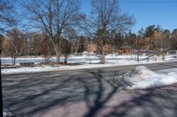 a street in a snow covered area with trees, a small building and a fence