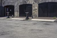 three parking meters sitting next to each other in a parking lot with brick walls and doors