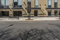 a building with windows and trees on a street in front of it with snow and no leaves