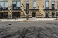 a building with windows and trees on a street in front of it with snow and no leaves