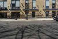 a building with windows and trees on a street in front of it with snow and no leaves