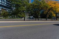 a road with cars in it and a yellow line on the street behind it, in front of a large building