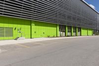 an empty road is outside of a green building with some green shutters on it