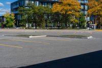 there is a black car on the street near some buildings and trees with yellow leaves