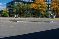 there is a black car on the street near some buildings and trees with yellow leaves