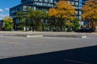 there is a black car on the street near some buildings and trees with yellow leaves