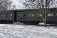 a snow covered field next to train cars in the middle of winter time on tracks