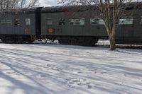 a snow covered field next to train cars in the middle of winter time on tracks