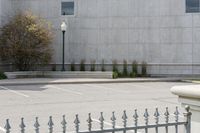 a building with parking lot and several windows on it's facade as seen through a wrought iron fence