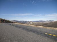 an open road leads up to a valley with a steep hillside in the background and blue skies above