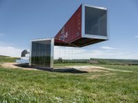 a shipping container is suspended from the side with its doors open on top of it, in front of a grassy field with a large blue sky background