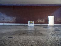 a door is open in an empty room with no windows, with cobblestone floor and red brick walls