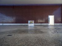 a door is open in an empty room with no windows, with cobblestone floor and red brick walls