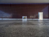 a door is open in an empty room with no windows, with cobblestone floor and red brick walls