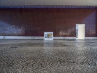 a door is open in an empty room with no windows, with cobblestone floor and red brick walls