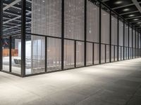 the glass windows with the doors in the building are open and there are a table, chairs and umbrellas on the concrete floor