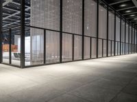 the glass windows with the doors in the building are open and there are a table, chairs and umbrellas on the concrete floor