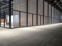 the glass windows with the doors in the building are open and there are a table, chairs and umbrellas on the concrete floor