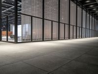 the glass windows with the doors in the building are open and there are a table, chairs and umbrellas on the concrete floor