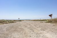 an open gravel road with a sign next to it and some grass in the field