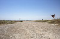 an open gravel road with a sign next to it and some grass in the field