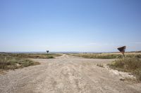 an open gravel road with a sign next to it and some grass in the field