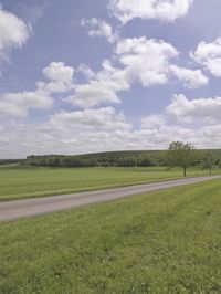a lone road in an open green field near the countryside of a valley and some hills