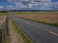 an open highway leading down a wide open plain towards the mountains and ocean, under cloudy skies