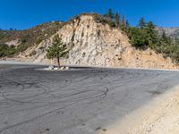 an empty empty parking lot next to a mountain road with a tree on a hill