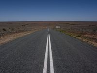 the middle section of an empty open road with the line white painted on it and a sign in the distance