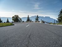 an empty open road with trees, grass and mountains in the distance on a sunny day