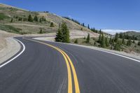 the open road with yellow stripe on the edge is surrounded by trees and snow capped mountains