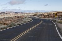 a wide open road in the middle of mountains and snow capped mountain tops in the distance