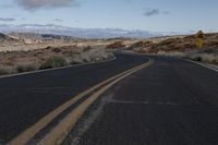 a wide open road in the middle of mountains and snow capped mountain tops in the distance