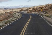 a wide open road in the middle of mountains and snow capped mountain tops in the distance